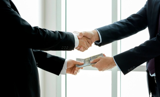 Businessmen making handshake while passing money - dealing &amp; bri